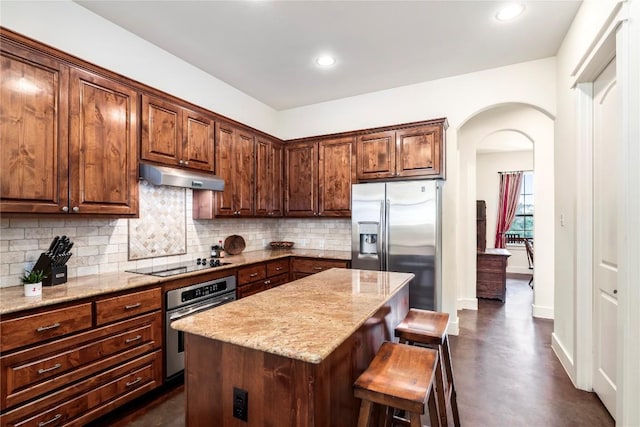 kitchen featuring a breakfast bar area, backsplash, stainless steel appliances, a center island, and light stone counters