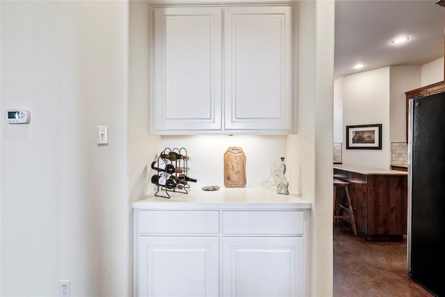 bar with backsplash, white cabinets, and stainless steel refrigerator