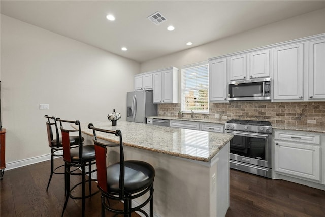 kitchen with a breakfast bar, tasteful backsplash, dark hardwood / wood-style floors, stainless steel appliances, and white cabinets