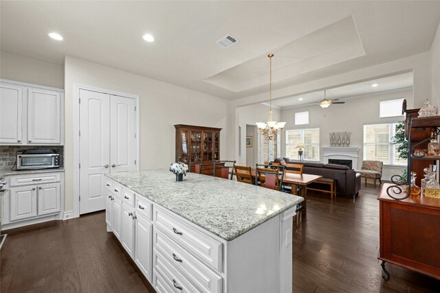 204 Delfino Cir, Lakeway, TX 78734 - kitchen featuring a fireplace, a center island, a tray ceiling, light stone counters, and white cabinets