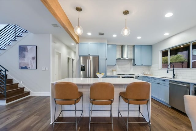 kitchen featuring wall chimney exhaust hood, appliances with stainless steel finishes, decorative light fixtures, and sink