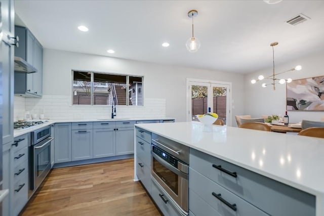 kitchen featuring sink, light hardwood / wood-style flooring, pendant lighting, stainless steel appliances, and decorative backsplash