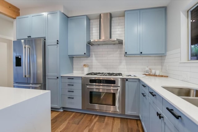 kitchen featuring wood-type flooring, appliances with stainless steel finishes, decorative backsplash, and wall chimney exhaust hood