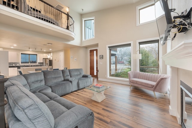 living room featuring a towering ceiling, a healthy amount of sunlight, and hardwood / wood-style floors