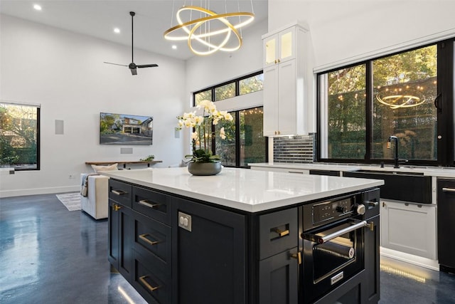 kitchen with a towering ceiling, white cabinetry, sink, hanging light fixtures, and black appliances