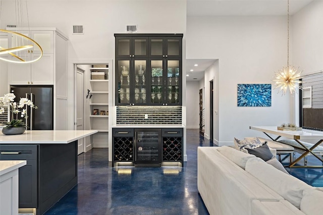 bar featuring black refrigerator, a towering ceiling, decorative light fixtures, and a chandelier