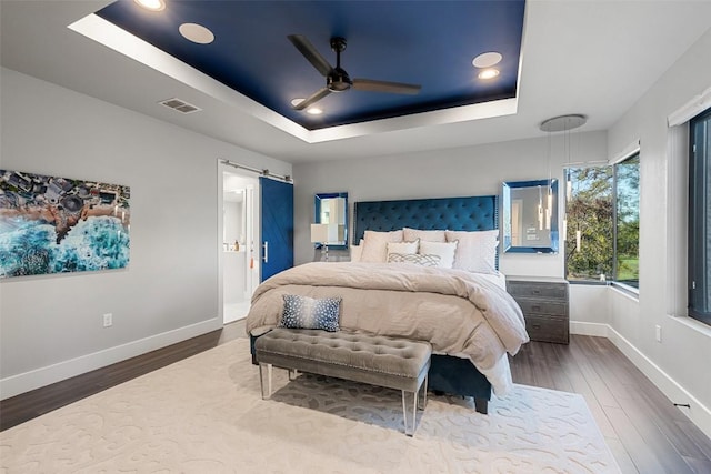 bedroom with a raised ceiling, a barn door, hardwood / wood-style flooring, and ceiling fan