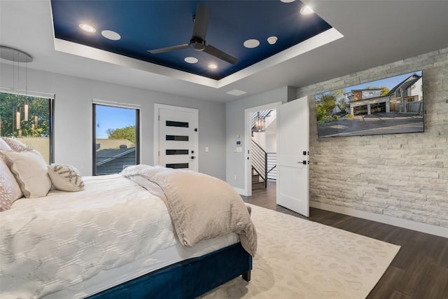 bedroom featuring dark hardwood / wood-style floors, access to outside, a raised ceiling, and ceiling fan