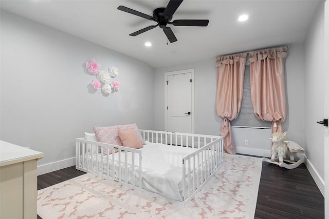 bedroom with dark wood-type flooring, ceiling fan, and a nursery area