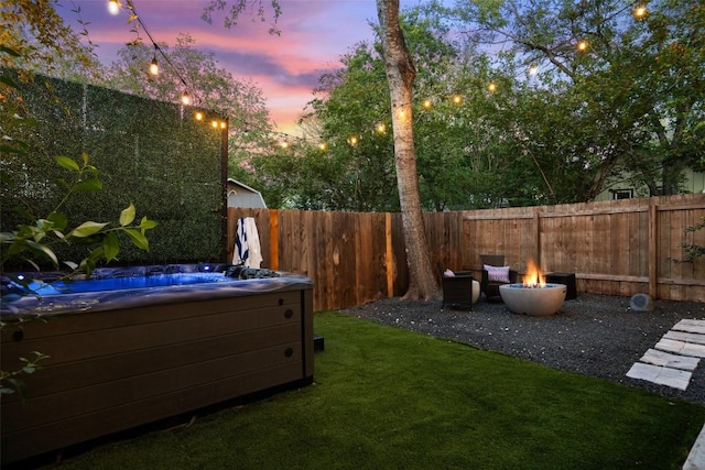 yard at dusk with a hot tub and an outdoor fire pit