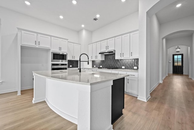 586 Biscayne Bay Bnd, Kyle, TX 78640 - kitchen featuring built in microwave, stainless steel oven, arched walkways, white cabinets, and black stovetop