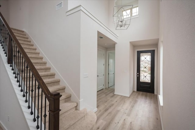 entrance foyer with visible vents, a towering ceiling, light wood finished floors, baseboards, and a chandelier