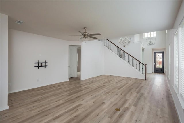 unfurnished living room with light wood finished floors, visible vents, ceiling fan with notable chandelier, and stairs