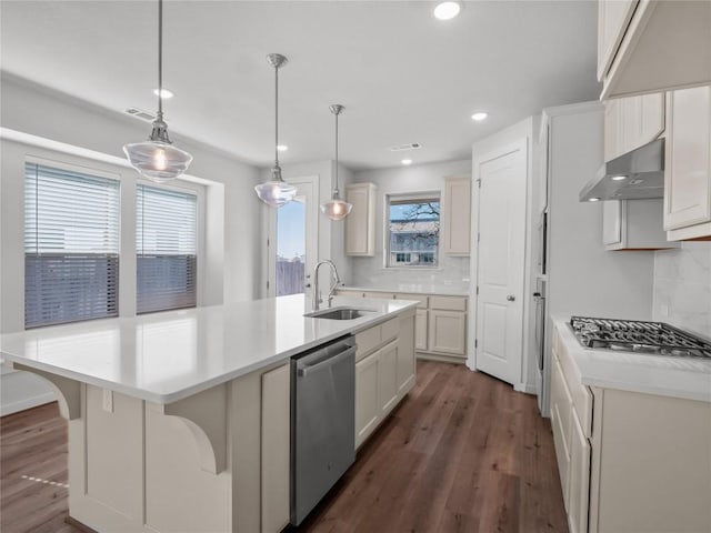 kitchen with dark wood finished floors, a sink, stainless steel appliances, light countertops, and wall chimney exhaust hood