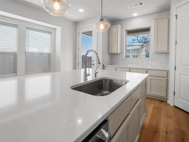 kitchen featuring tasteful backsplash, visible vents, pendant lighting, light wood-style floors, and a sink