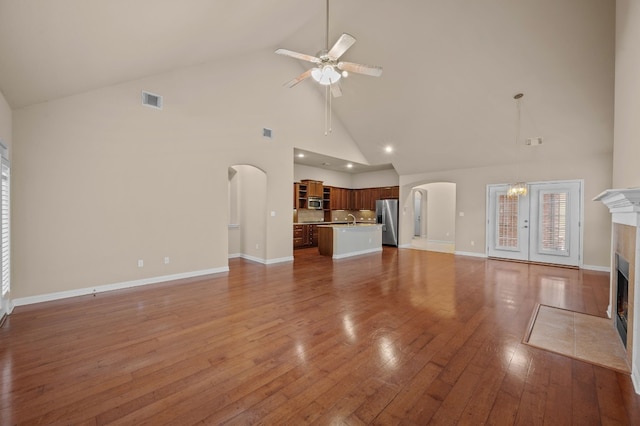 unfurnished living room featuring sink, ceiling fan, hardwood / wood-style floors, high vaulted ceiling, and a tiled fireplace