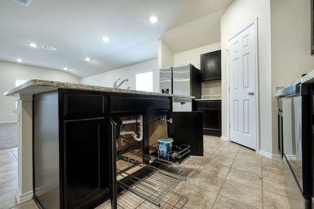 kitchen featuring light tile patterned flooring, lofted ceiling, stainless steel fridge, and light stone countertops