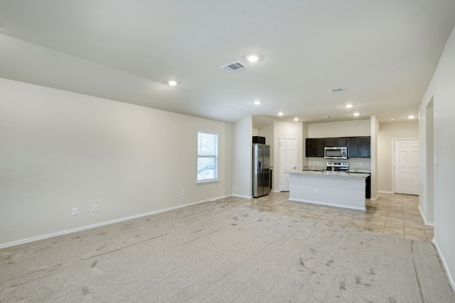 kitchen with stainless steel appliances, light stone countertops, a kitchen island with sink, and light carpet