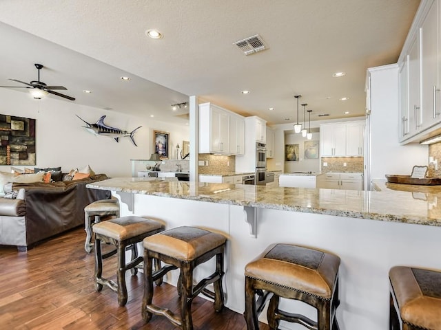 kitchen featuring pendant lighting, white cabinetry, kitchen peninsula, light stone countertops, and stainless steel double oven