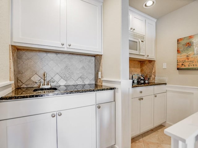 kitchen featuring light tile patterned flooring, white cabinetry, sink, dark stone countertops, and decorative backsplash