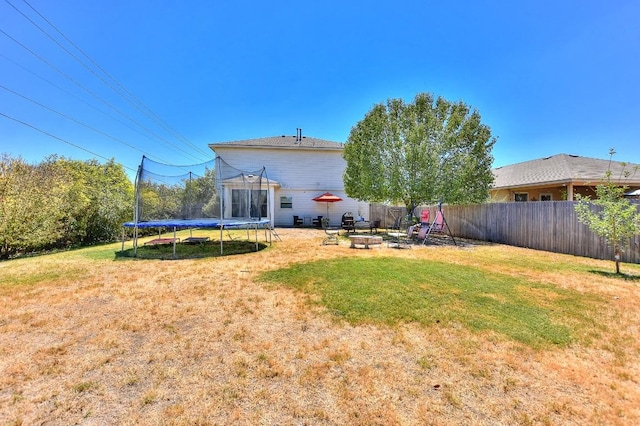 back of property featuring a yard, a trampoline, and an outdoor fire pit