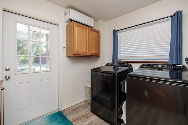 laundry area featuring cabinets, an AC wall unit, washing machine and clothes dryer, and light hardwood / wood-style flooring