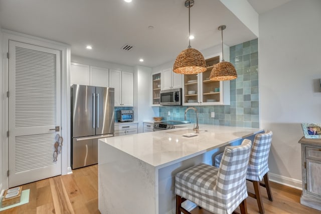 kitchen with a breakfast bar, hanging light fixtures, kitchen peninsula, stainless steel appliances, and white cabinets