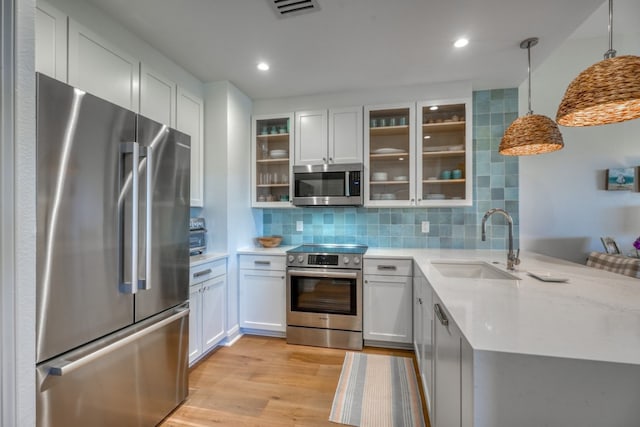 kitchen featuring sink, light hardwood / wood-style flooring, appliances with stainless steel finishes, hanging light fixtures, and white cabinets