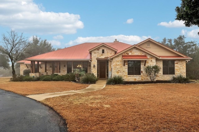 view of front of property featuring metal roof, stone siding, a chimney, and a front lawn