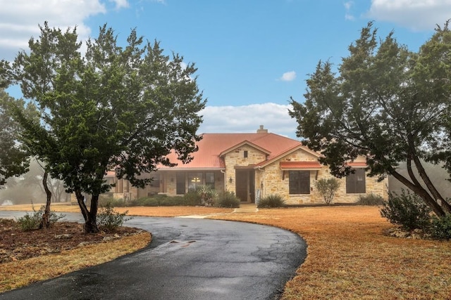 view of front facade featuring aphalt driveway, a front lawn, stone siding, and a chimney