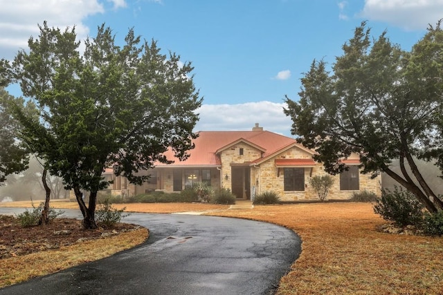 view of front of home with stone siding, curved driveway, a chimney, and a front yard