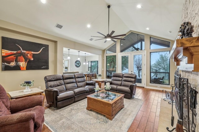 living room featuring high vaulted ceiling, a stone fireplace, light wood-type flooring, and a wealth of natural light