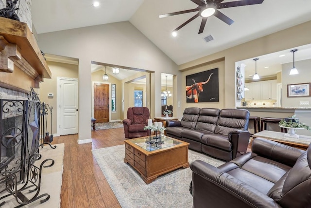 living area featuring light wood finished floors, visible vents, a large fireplace, high vaulted ceiling, and a ceiling fan