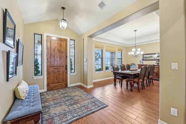 foyer entrance with wood finished floors, visible vents, baseboards, lofted ceiling, and a notable chandelier