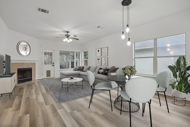 dining room featuring ceiling fan, a tile fireplace, and light wood-type flooring