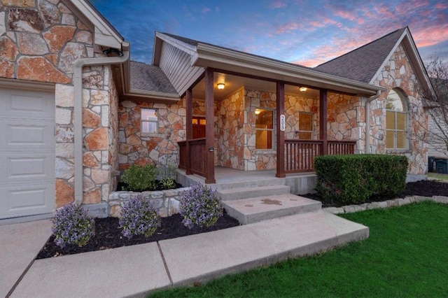 205 Errol Dr, Spicewood, TX 78669 - exterior entry at dusk featuring stone siding, covered porch, an attached garage, and roof with shingles