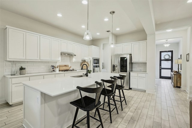 kitchen with stainless steel refrigerator with ice dispenser, pendant lighting, a center island with sink, and white cabinets