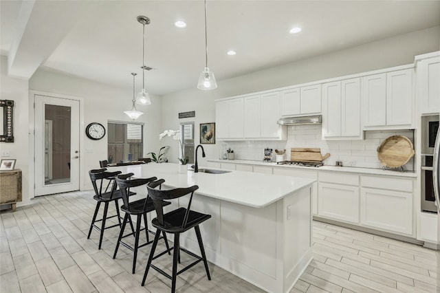 kitchen featuring pendant lighting, sink, tasteful backsplash, an island with sink, and white cabinets