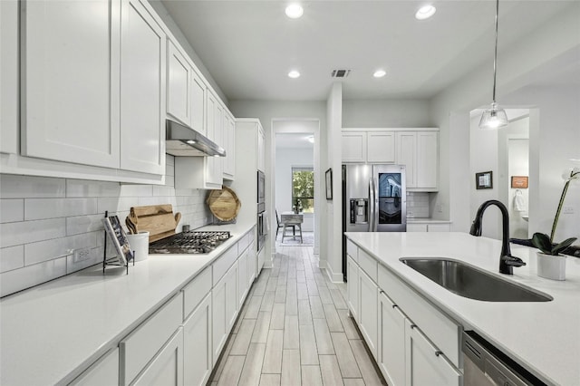 kitchen with sink, appliances with stainless steel finishes, white cabinetry, backsplash, and hanging light fixtures