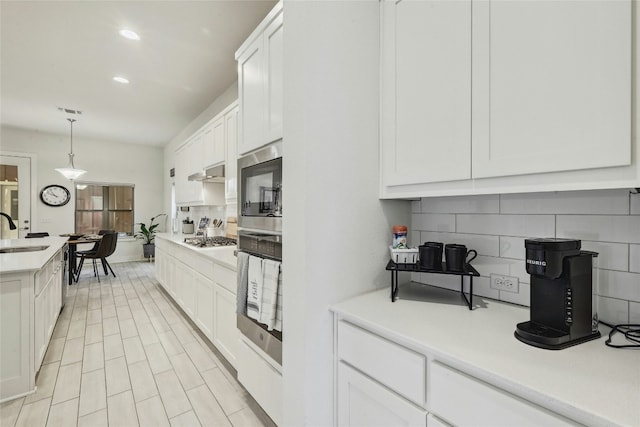 kitchen featuring sink, white cabinetry, hanging light fixtures, stainless steel appliances, and backsplash