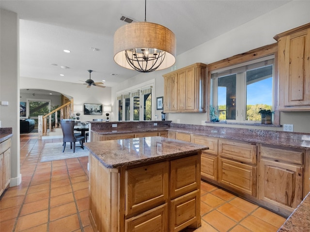 kitchen featuring light tile patterned flooring, decorative light fixtures, a kitchen island, and dark stone countertops