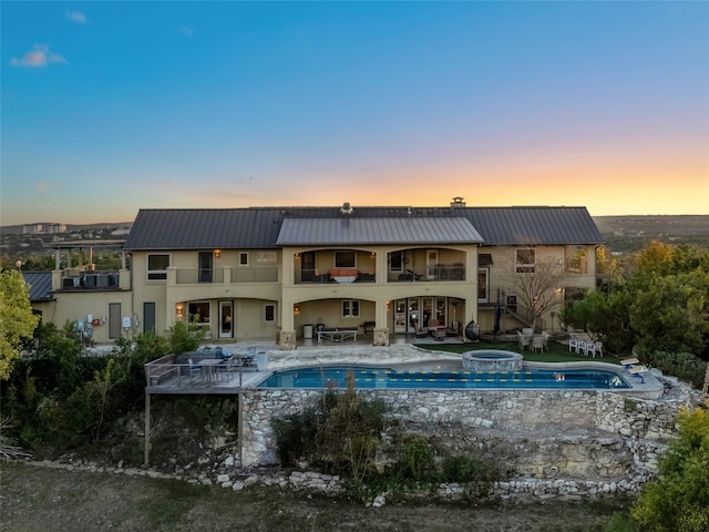 pool at dusk with a patio area and an in ground hot tub