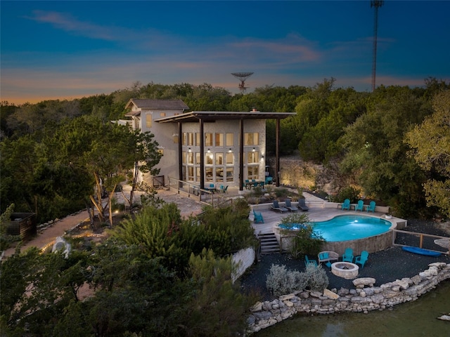 pool at dusk with an outdoor fire pit and a patio