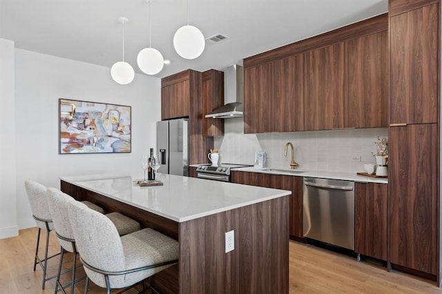 kitchen featuring wall chimney exhaust hood, sink, a center island, appliances with stainless steel finishes, and pendant lighting