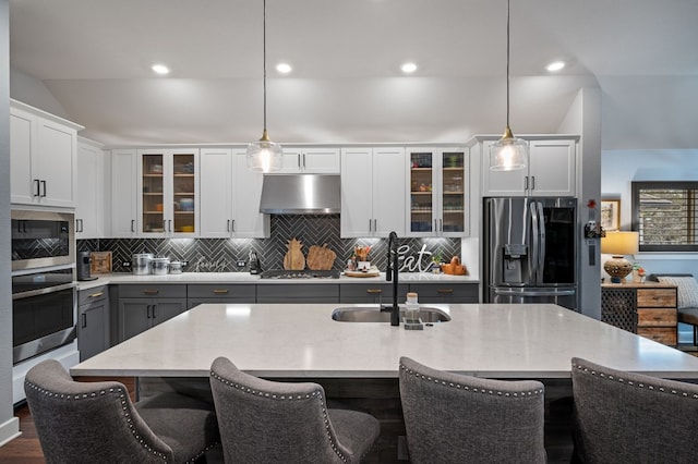 kitchen with stainless steel appliances, decorative light fixtures, sink, and a center island with sink