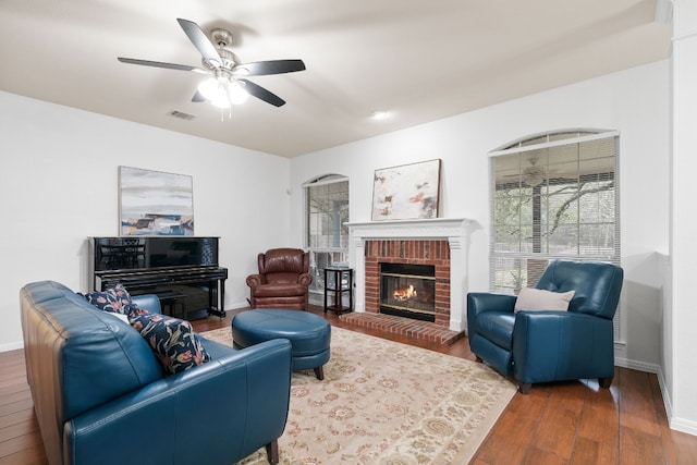 living room featuring ceiling fan, wood-type flooring, and a brick fireplace