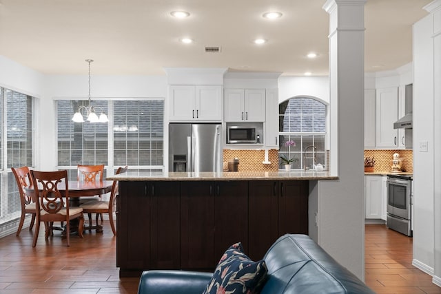 kitchen with pendant lighting, wall chimney range hood, stainless steel appliances, light stone counters, and white cabinets