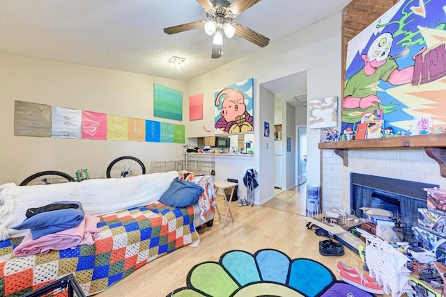 bedroom featuring wood-type flooring, a brick fireplace, ceiling fan, and a textured ceiling