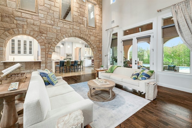 living room featuring baseboards, visible vents, dark wood finished floors, arched walkways, and a high ceiling