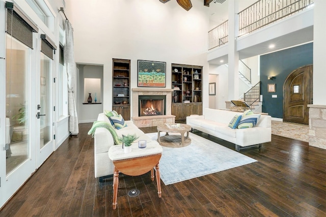 living area with a warm lit fireplace, stairs, a high ceiling, and dark wood-type flooring